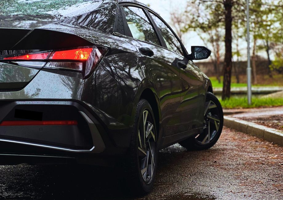 Rear view of a modern car on a rainy day, parked on a wet road surrounded by trees.